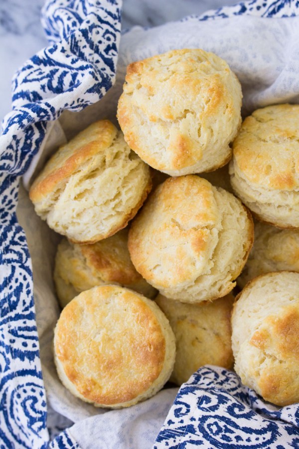 Golden brown, flaky homemade biscuits ready to serve in a napkin-lined bowl.