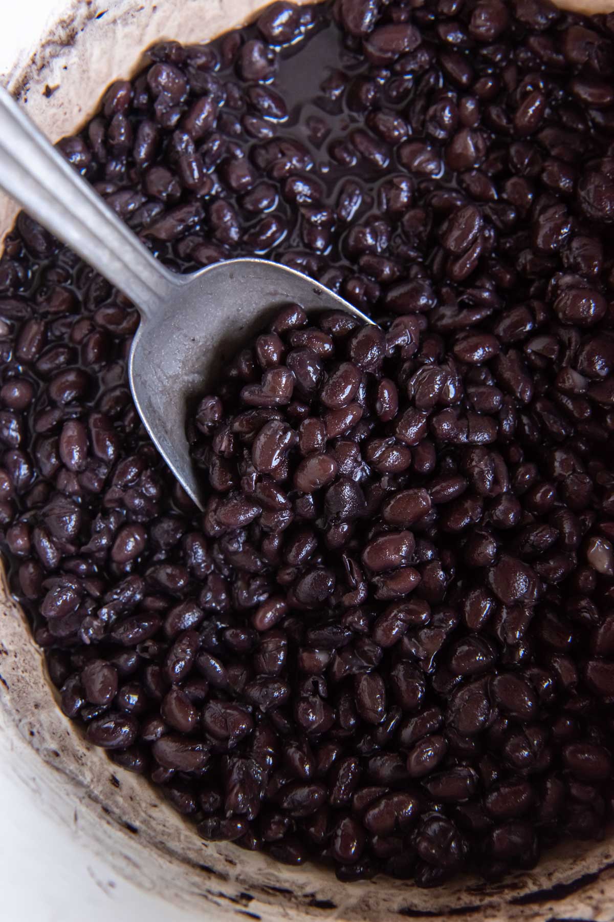 Close up of cooked black beans in pot with serving spoon.