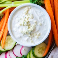 Blue cheese dressing in a small white bowl with fresh cut vegetables surrounding it.