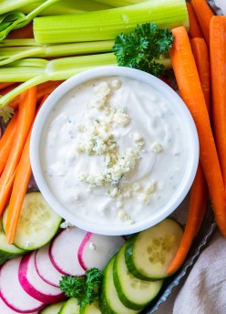 Blue cheese dressing in a small white bowl with fresh cut vegetables surrounding it.