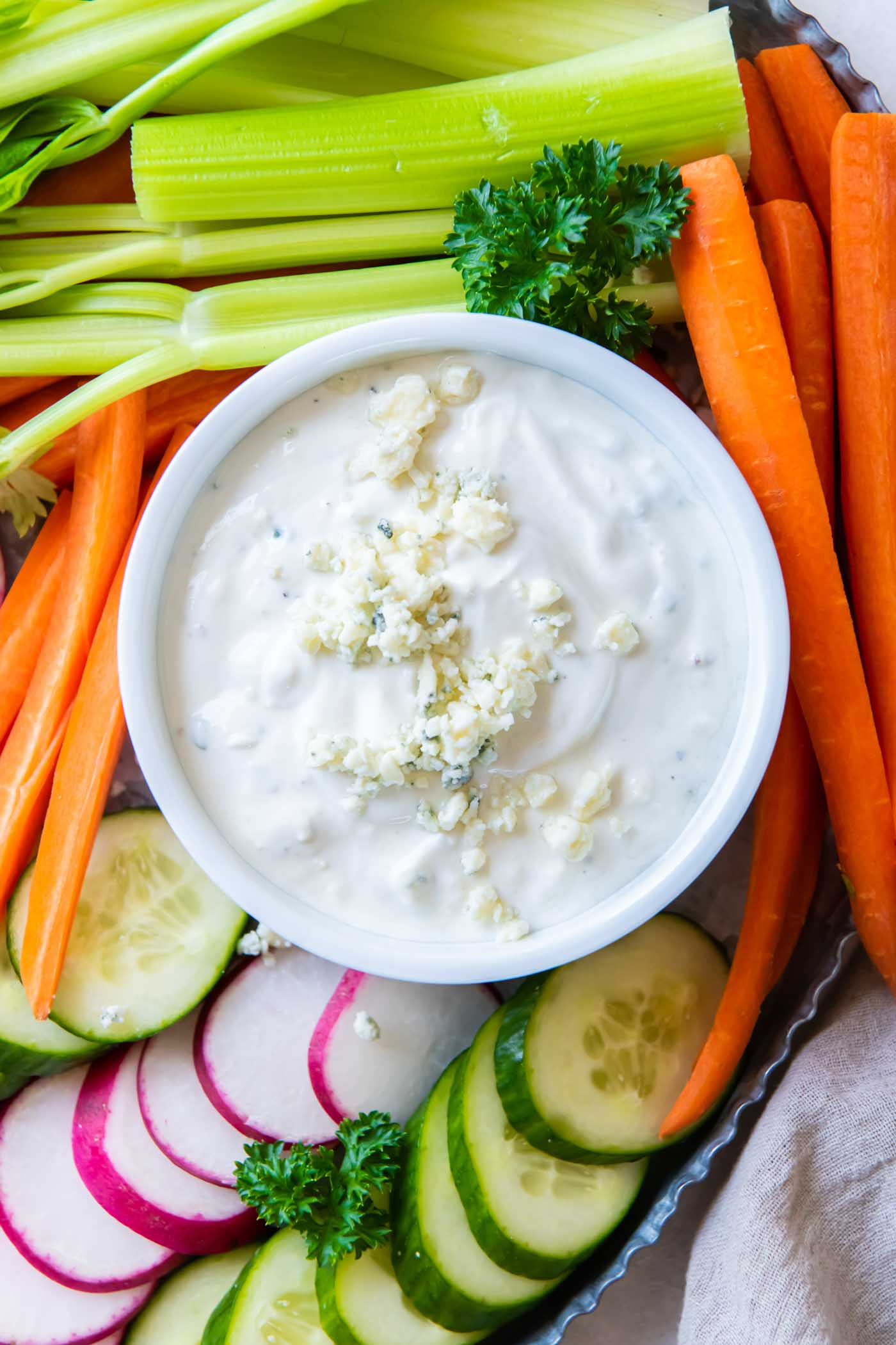 Blue cheese dressing in a small white bowl with fresh cut vegetables surrounding it.