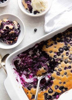 blueberry cobbler in a baking dish with a serving missing next to two dishes of cobbler