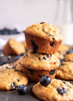 Two blueberry oatmeal muffins stacked on top of a muffin pan filled with muffins.