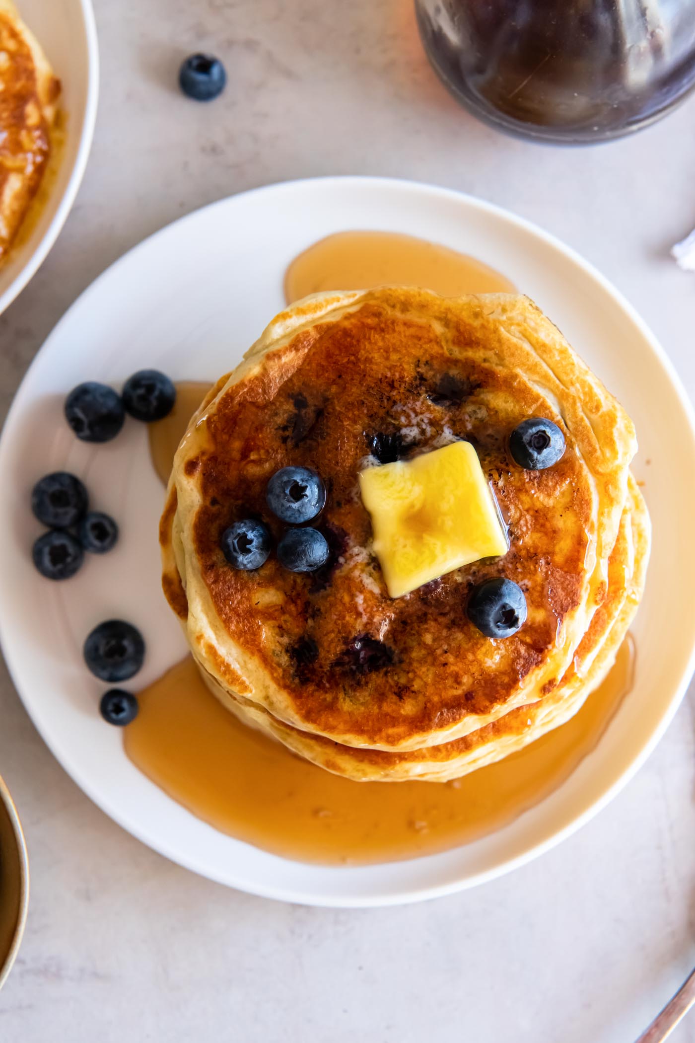 Stack of blueberry pancakes on a plate with butter, maple syrup and a few fresh blueberries.