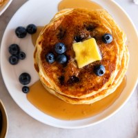 Stack of blueberry pancakes on a plate with butter, maple syrup and a few fresh blueberries.