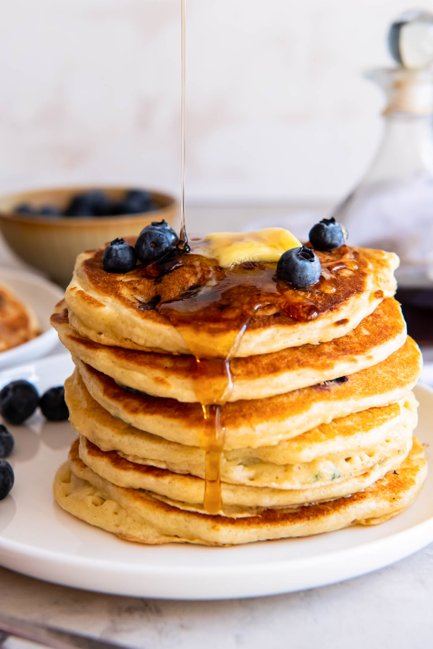 Side view of stack of blueberry pancakes with syrup being drizzled onto them.