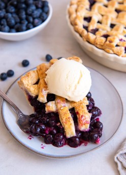 Slice of blueberry pie with scoop of vanilla ice cream on top.