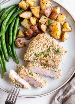 Partially sliced breaded pork chop served with roasted potatoes and green beans.