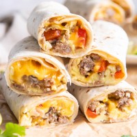 Breakfast burritos stacked on top of each other and cut in half so you can see the sausage, egg, cheese and veggies inside.