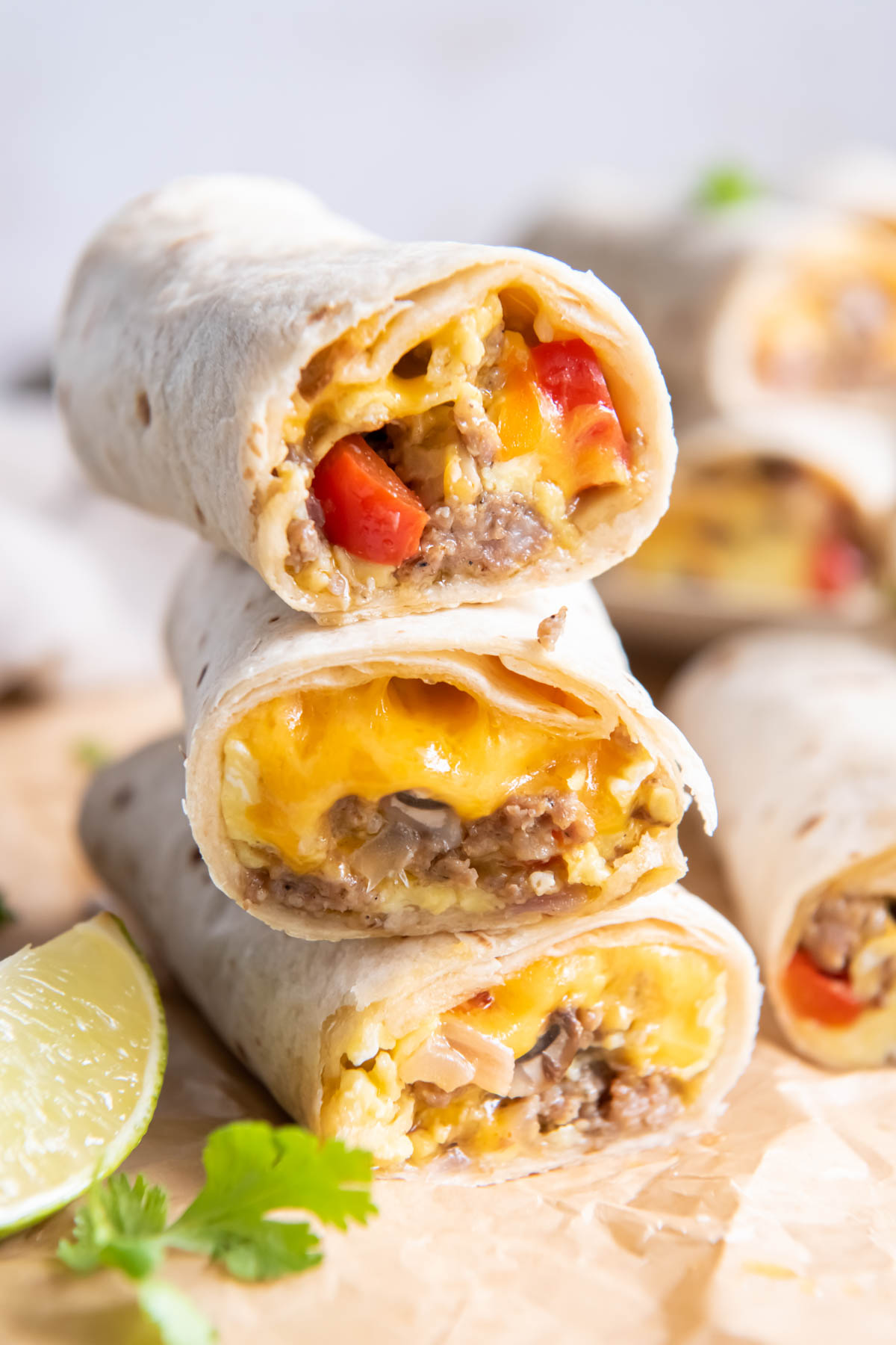 Three breakfast burritos stacked on top of each other and cut in half so you can see the sausage, eggs, cheese and vegetables inside.