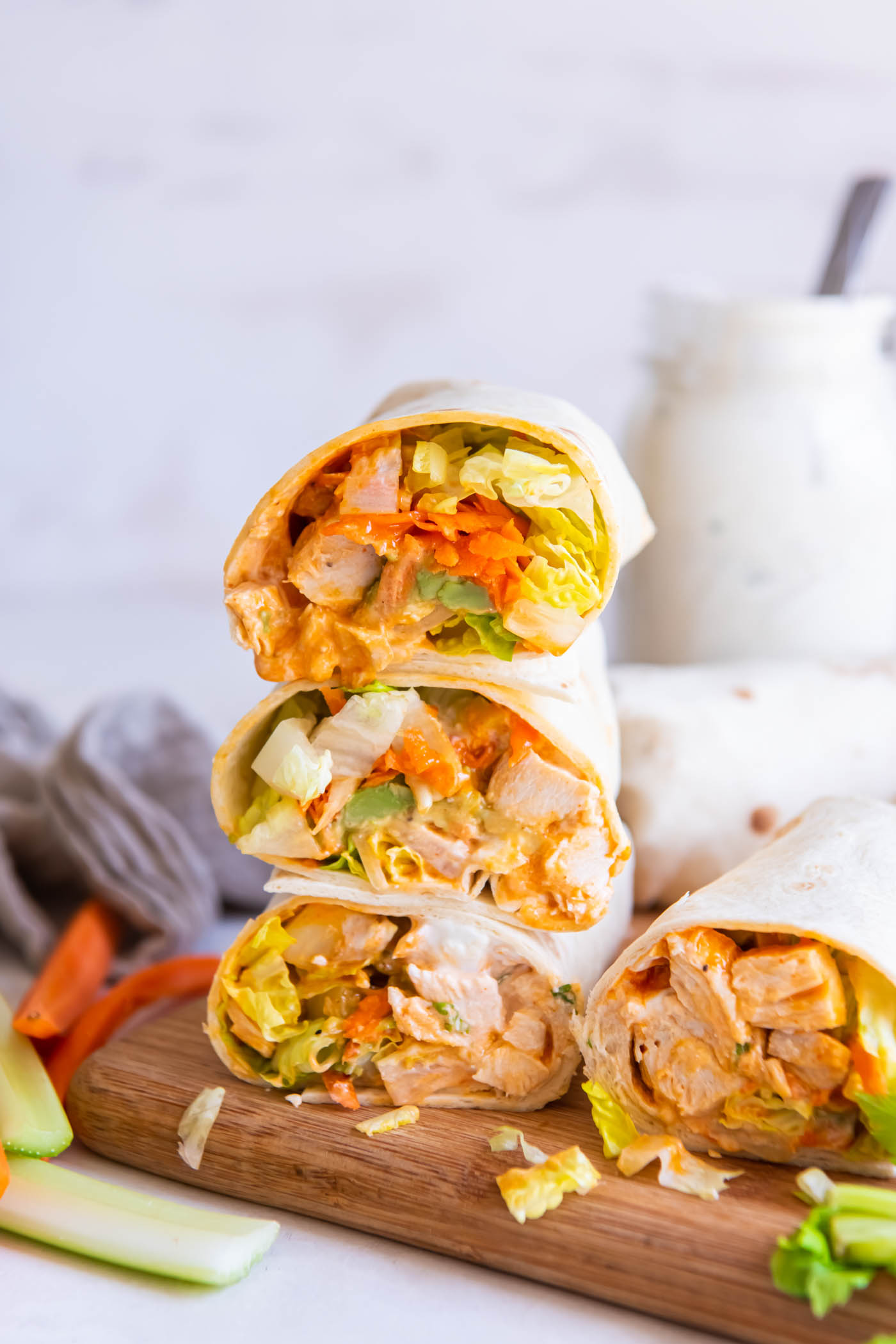 Three buffalo chicken wrap halves stacked on a cutting board.