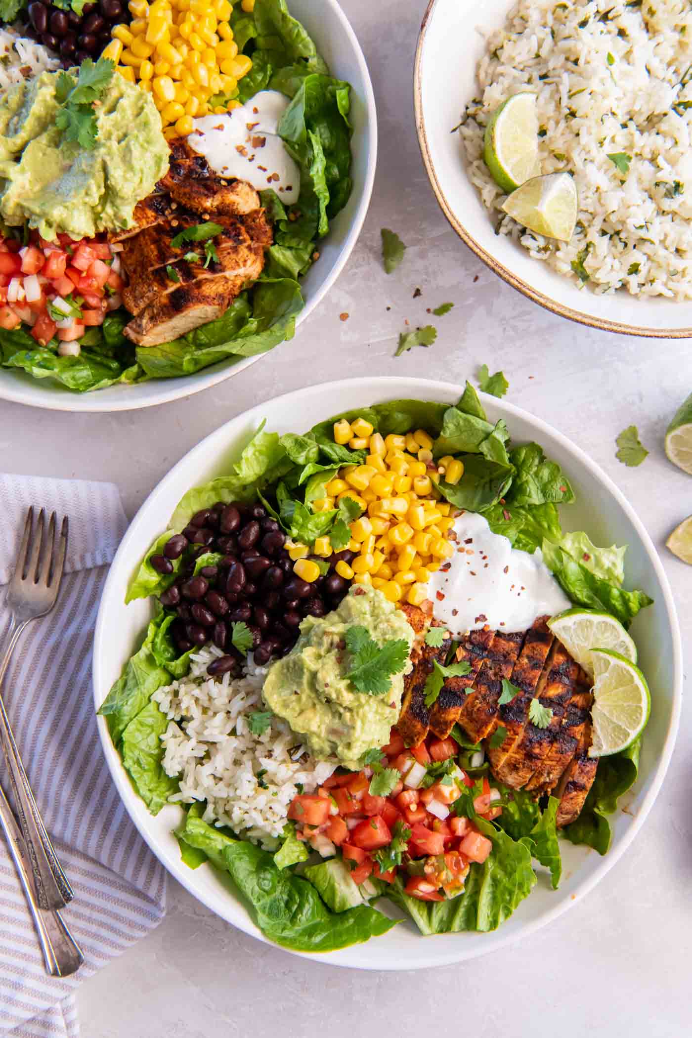 Two chicken burrito bowls with bowl of cilantro lime rice in the background.