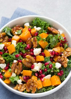Roasted butternut squash salad with candied walnuts, pomegranate seeds and goat cheese in a white bowl.