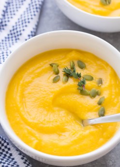 Butternut squash soup in a white bowl garnished with pepitas and thyme.