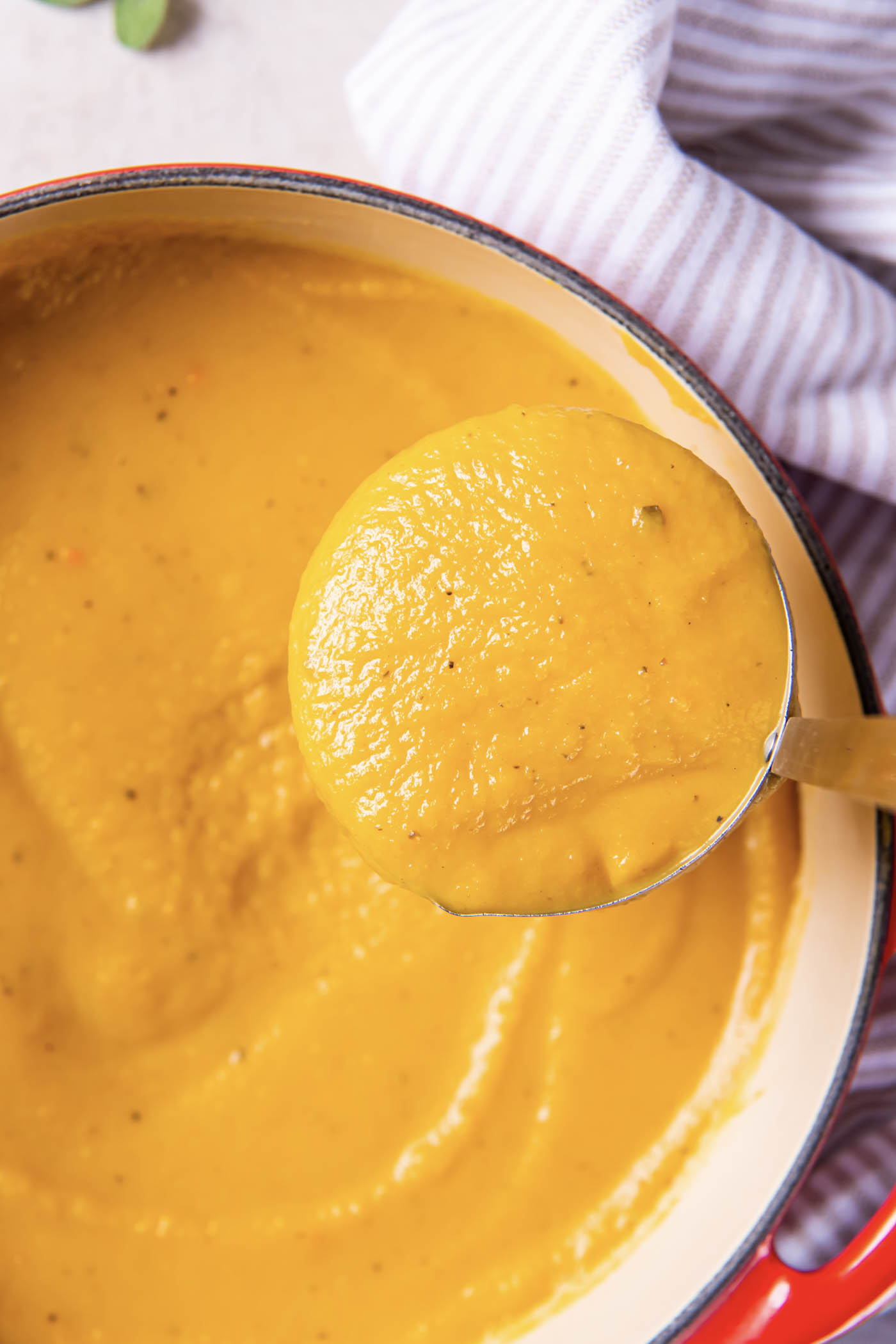 Butternut squash soup on a ladle held over pot of soup.