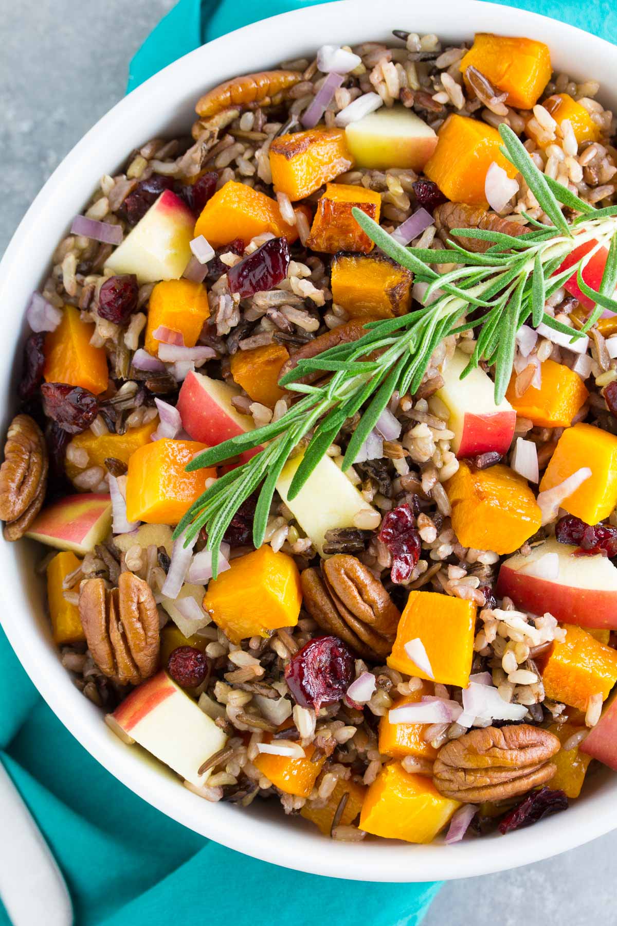 Wild rice salad with roasted butternut squash, apple, cranberries and apple cider dressing in white bowl.