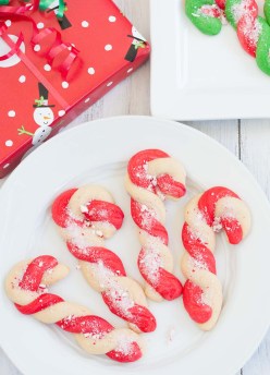 Candy cane cookies on a plate with wrapped presents in the background.