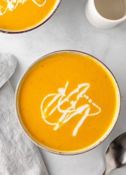 two bowls of carrot ginger soup drizzled with coconut milk