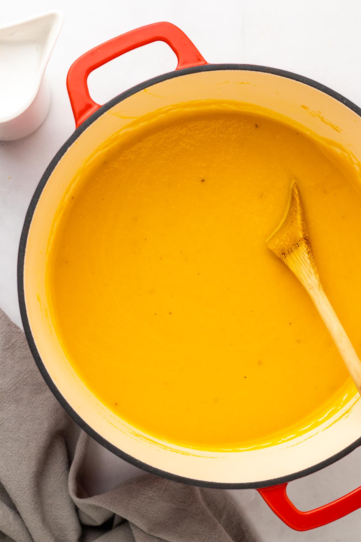Creamy carrot soup in dutch oven pot with wooden spoon.