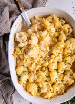Baked cauliflower mac and cheese in a casserole dish with serving spoon.