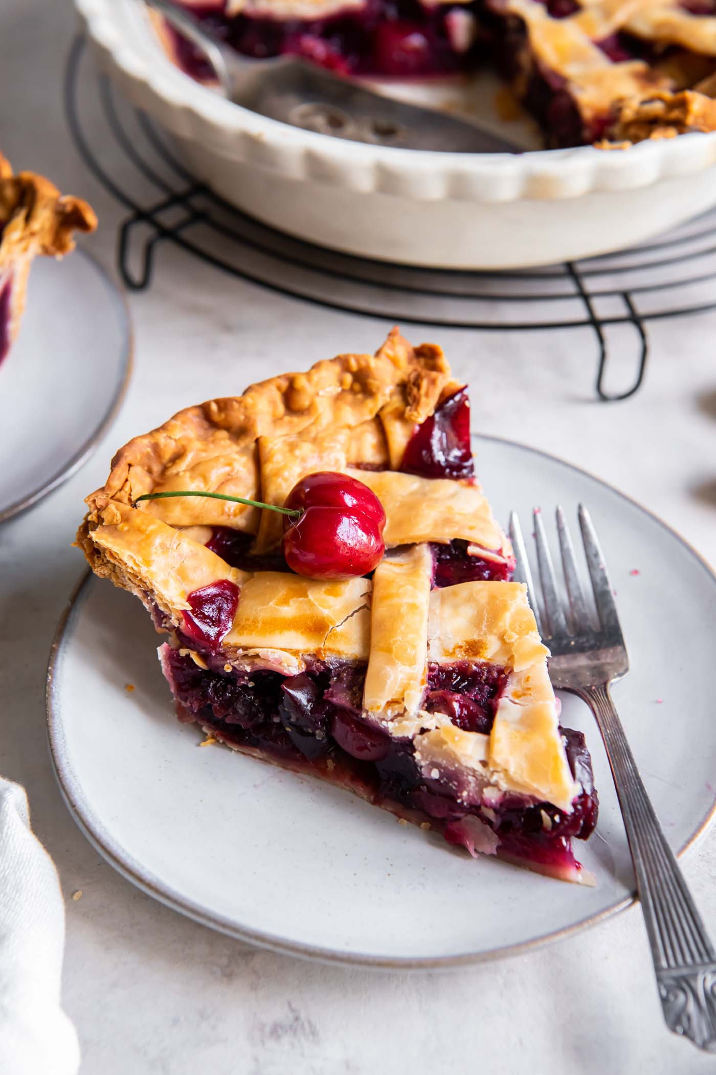 Slice of cherry pie on a small plate with a fork.