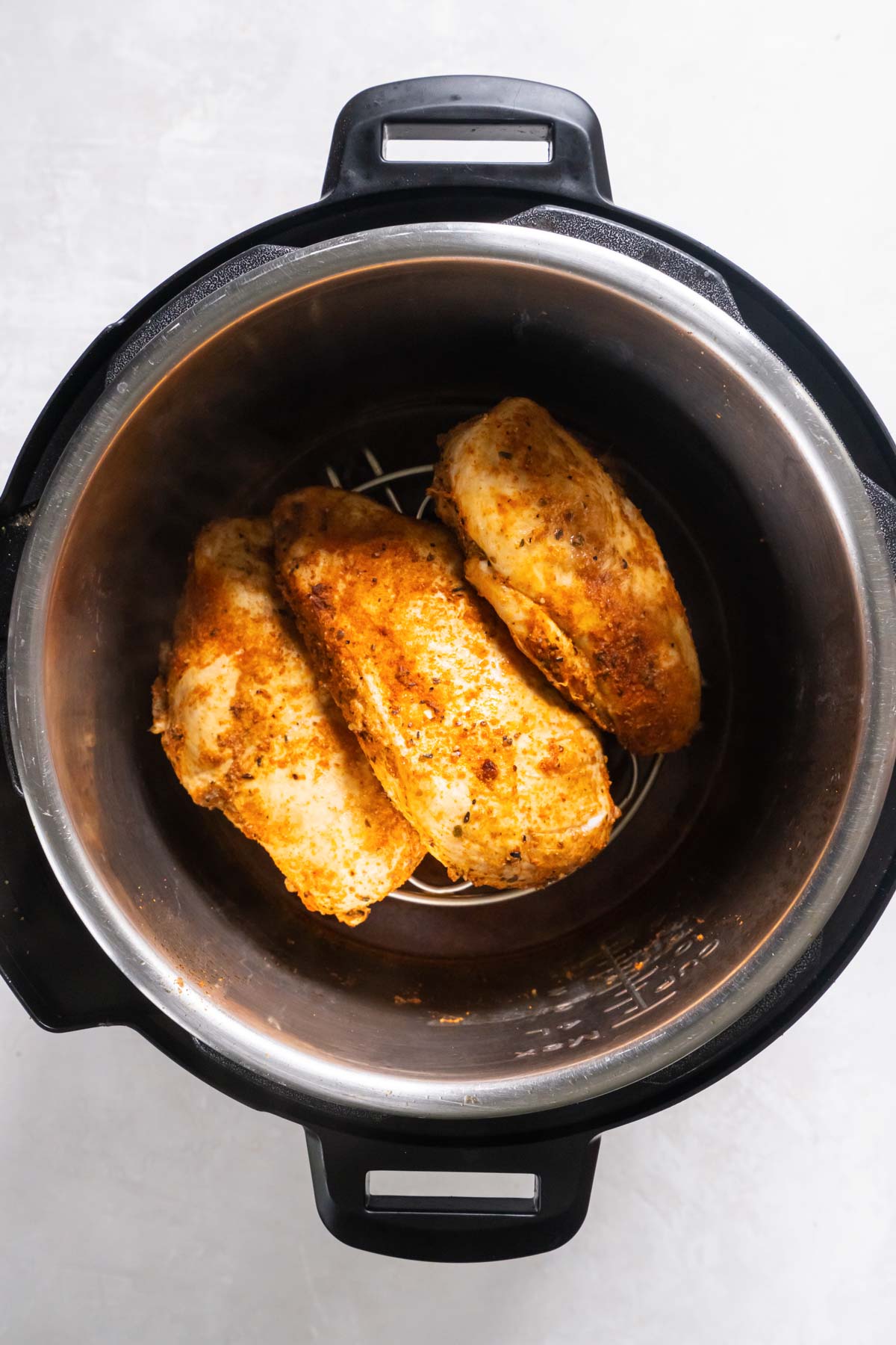 Three cooked chicken breasts on trivet in instant pot.