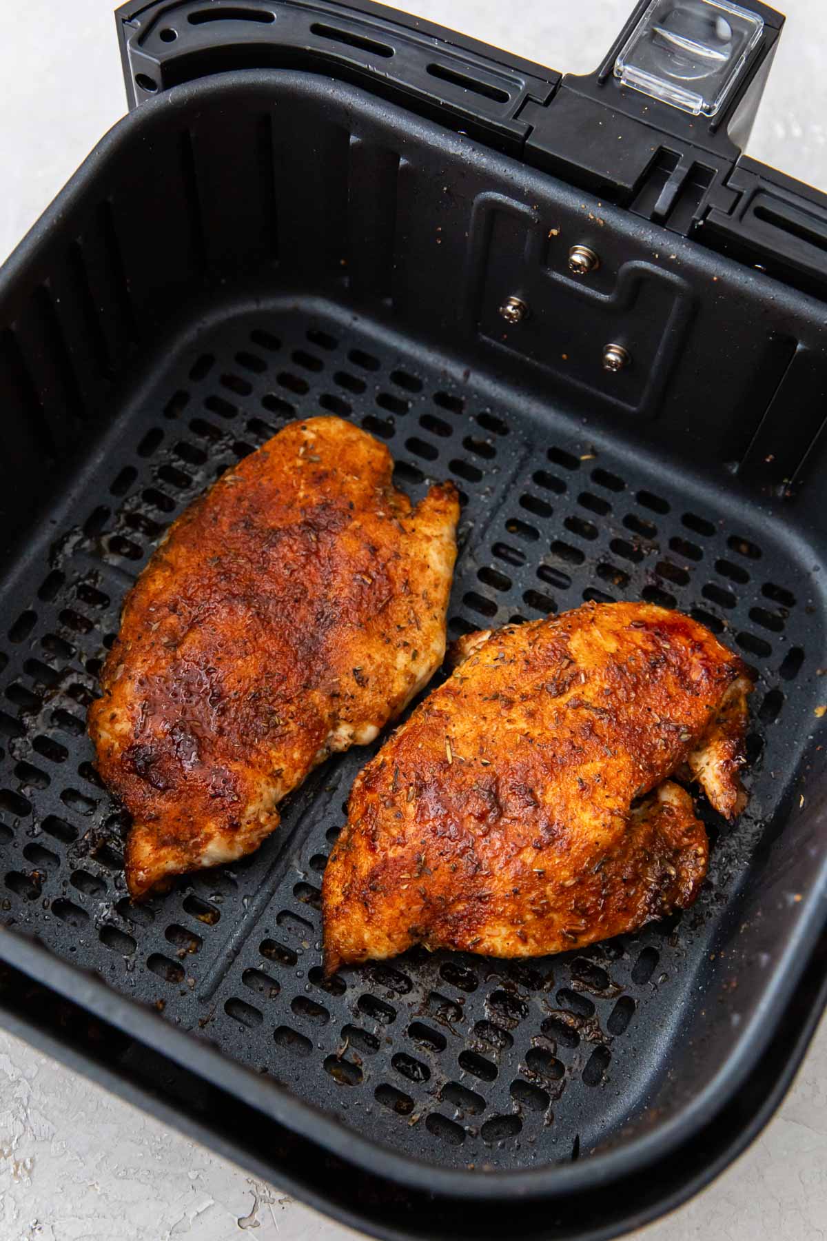 Two cooked chicken breasts in an air fryer.