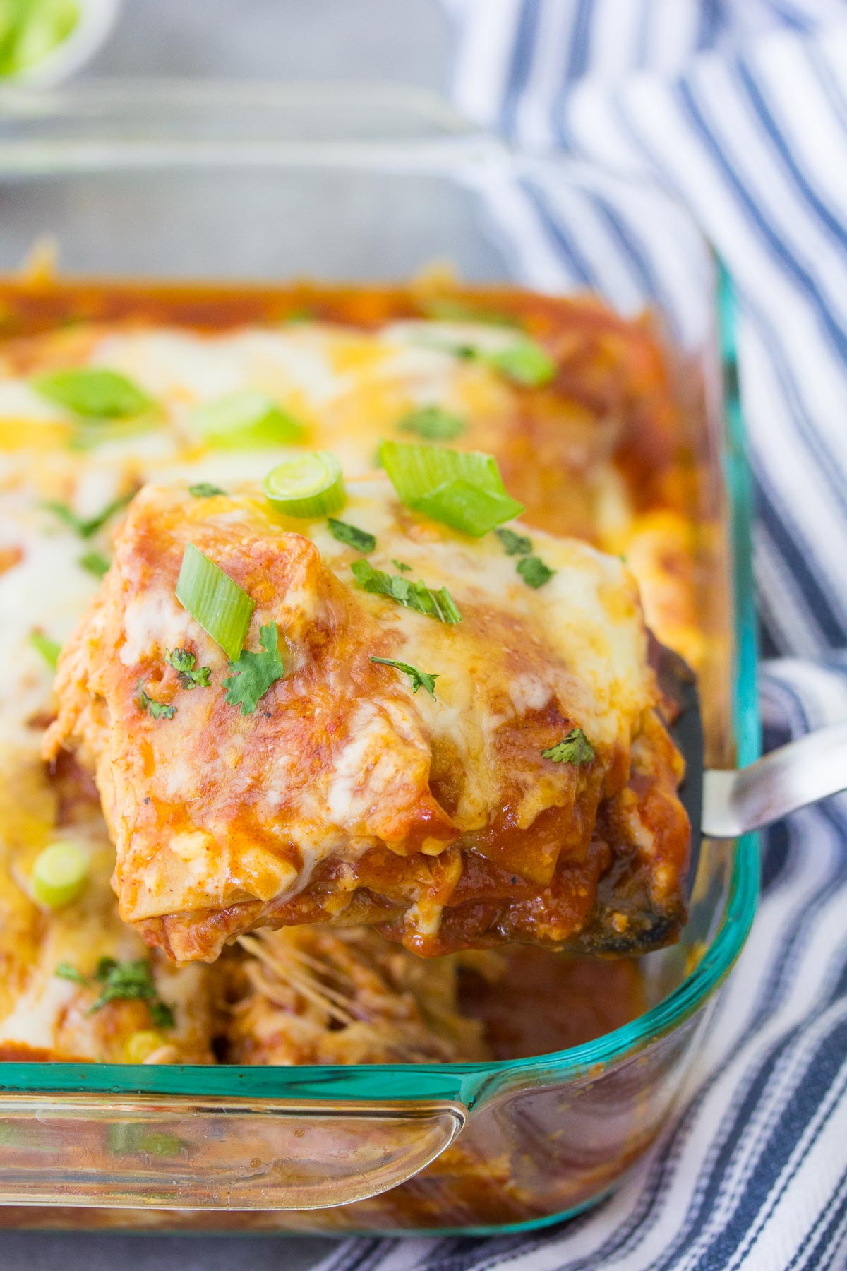 A slice of chicken enchilada casserole on a spatula, held over the casserole dish.