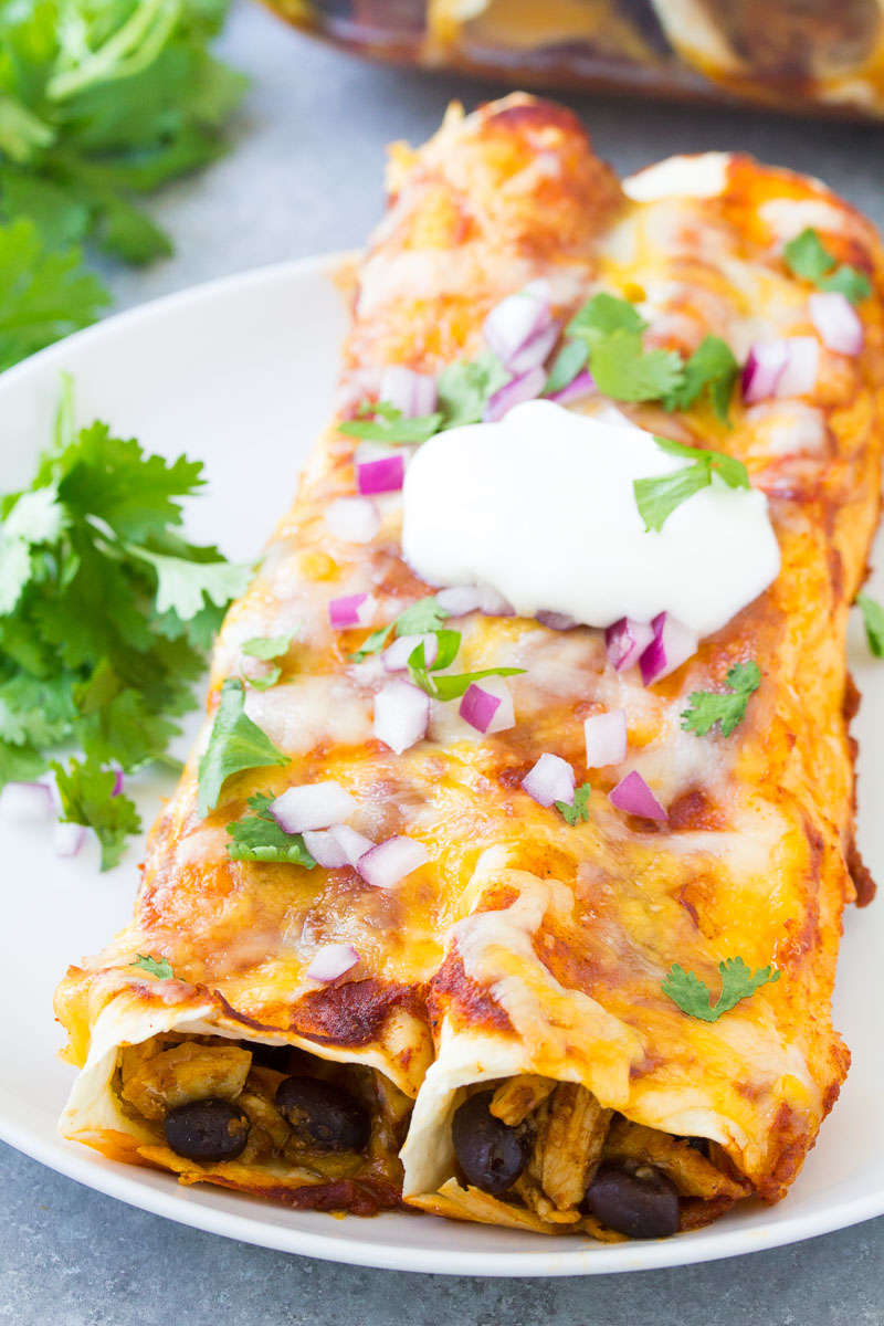 Two enchiladas on a plate topped with cilantro, red onion and sour cream.