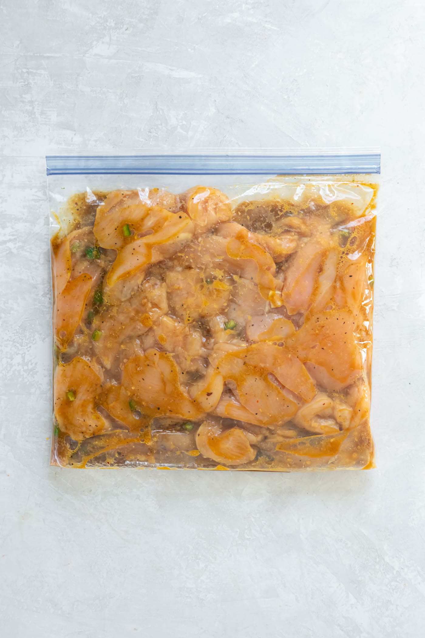 Sliced chicken breast and marinade in a sealed zip-top plastic bag.