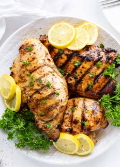 three marinated grilled chicken breasts on a plate with lemon slices and parsley