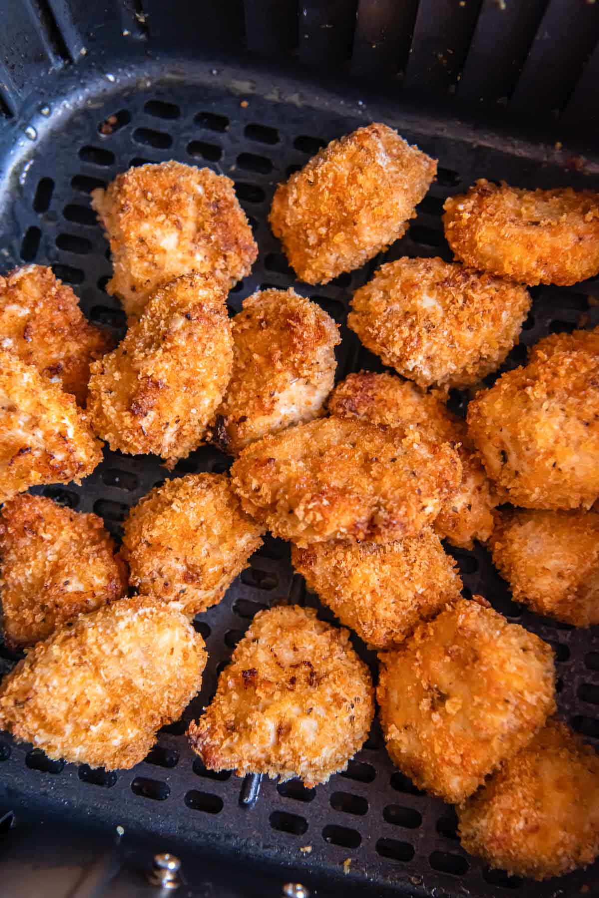 Cooked chicken nuggets stacked in air fryer basket.