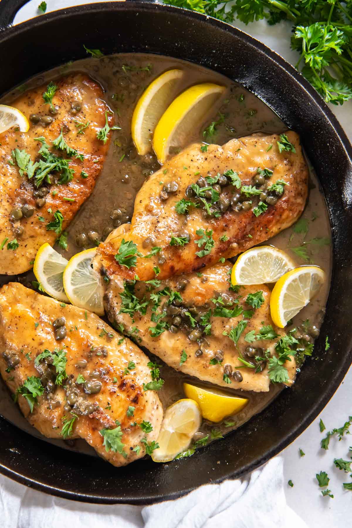 Chicken piccata with fresh parsley and lemon slices in a cast iron skillet.