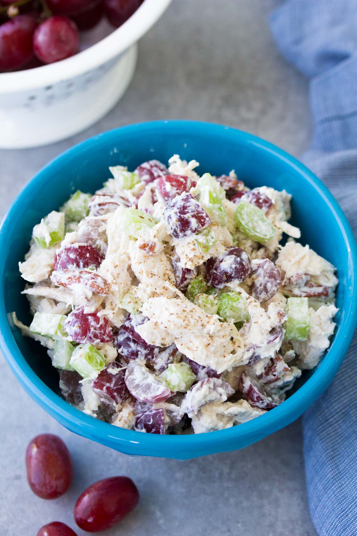 Chicken salad with grapes in a blue bowl with grapes in the background.