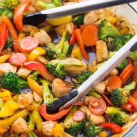 Chicken stir fry in a skillet with tongs.