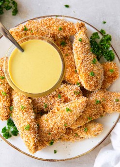 Chicken tenders stacked on a plate with a dish of honey mustard.