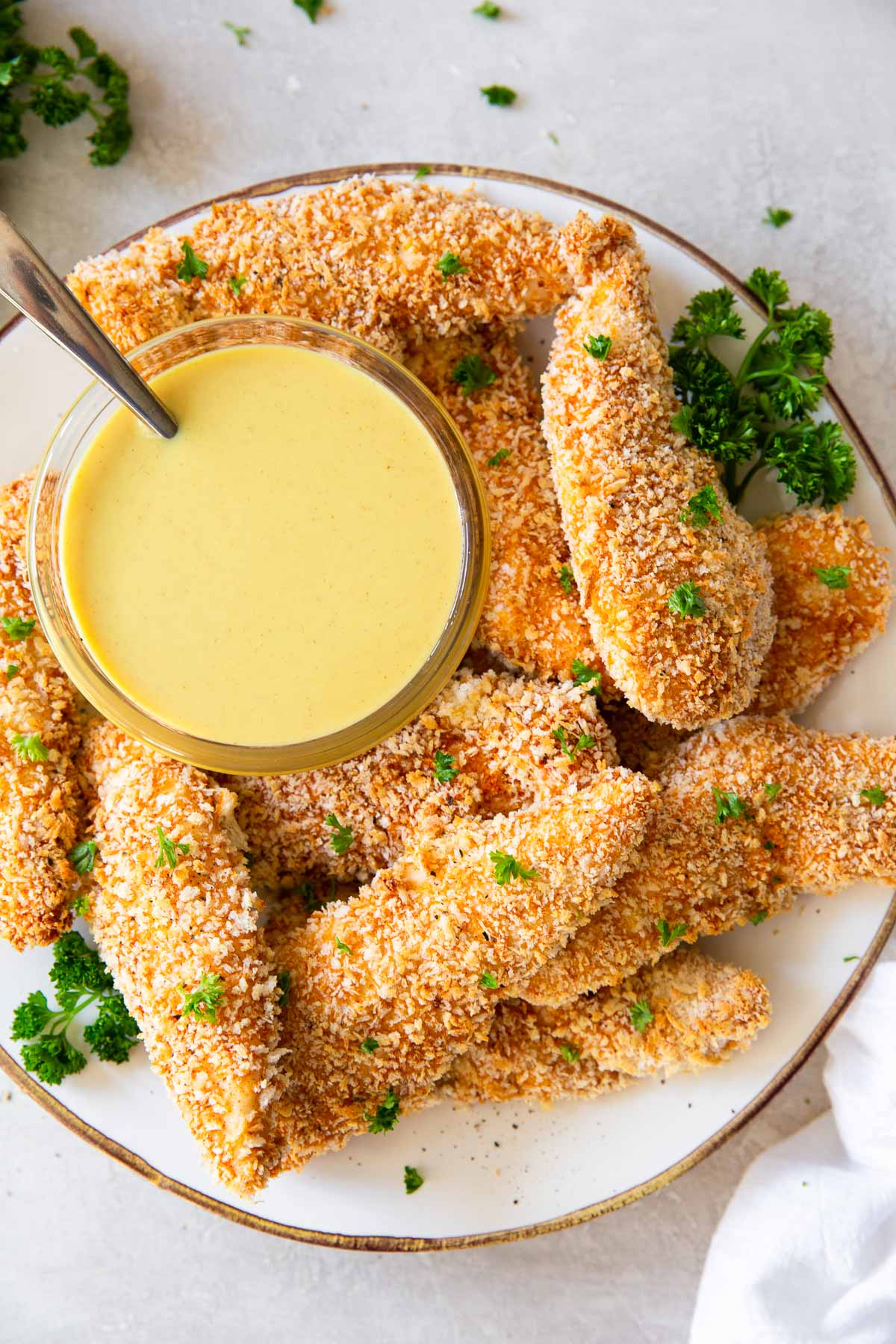Chicken tenders stacked on a plate with a dish of honey mustard.