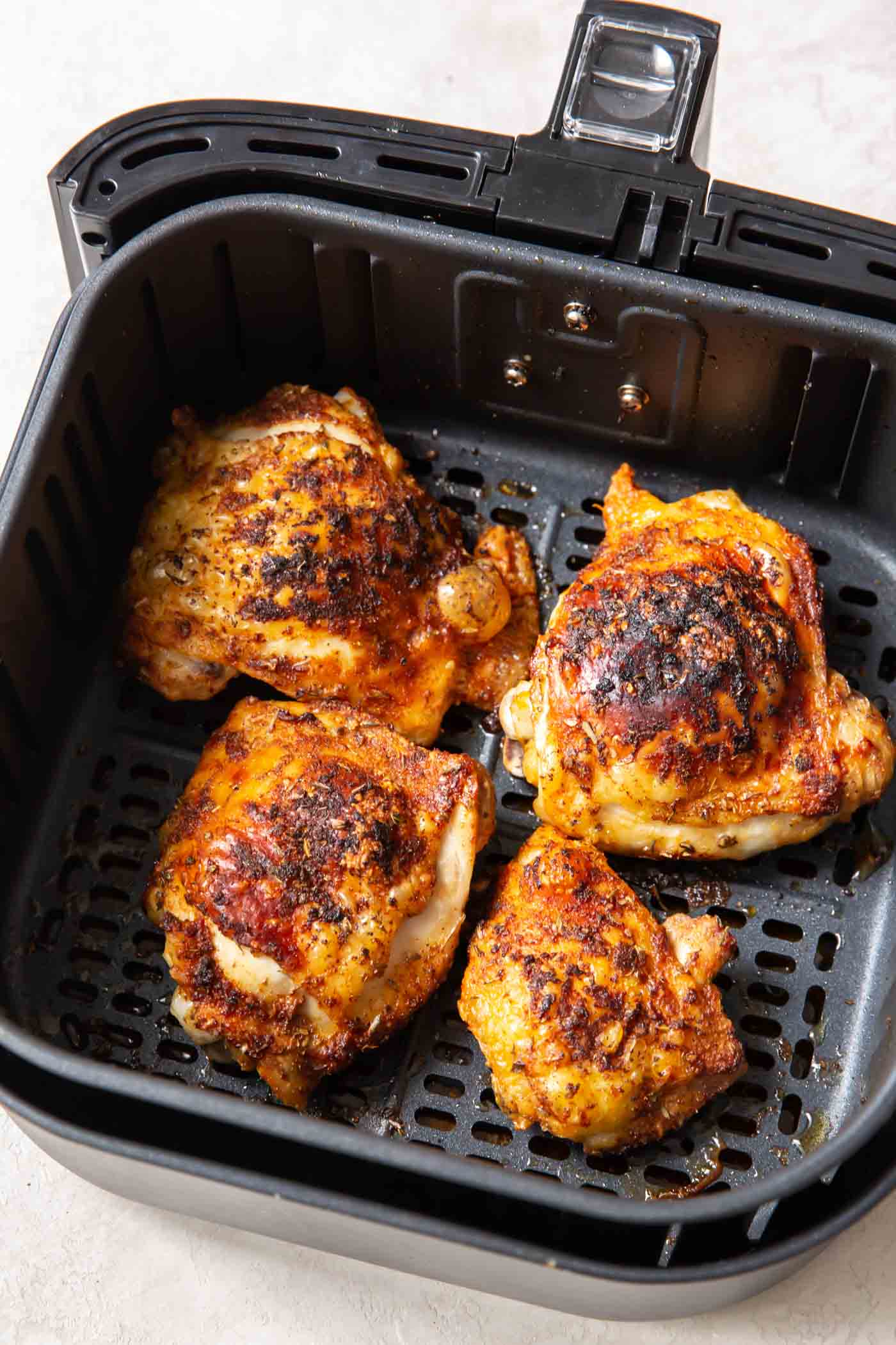 Four cooked bone-in chicken thighs in air fryer basket.