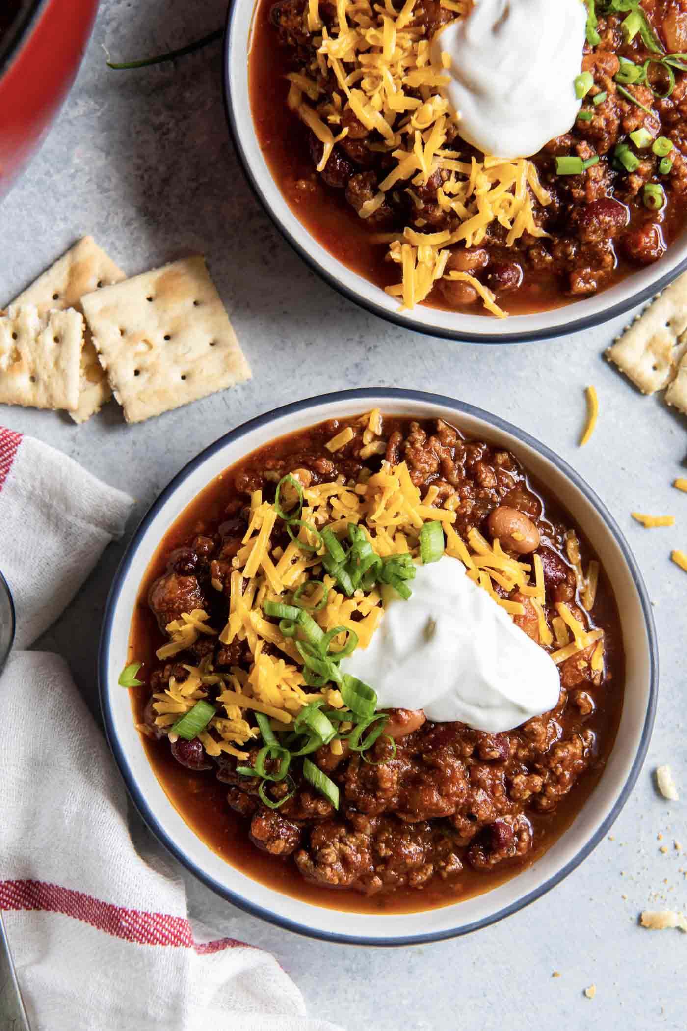 Two bowls of chili with cheese, sour cream and green onions.
