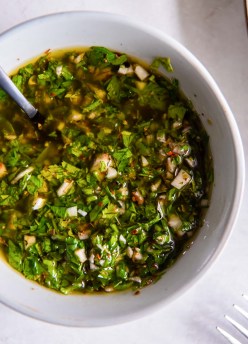 Chimichurri sauce in a white bowl with a spoon.