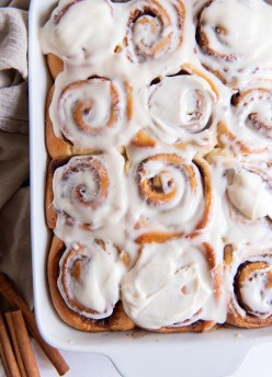 Cinnamon rolls with cream cheese frosting in white baking dish.