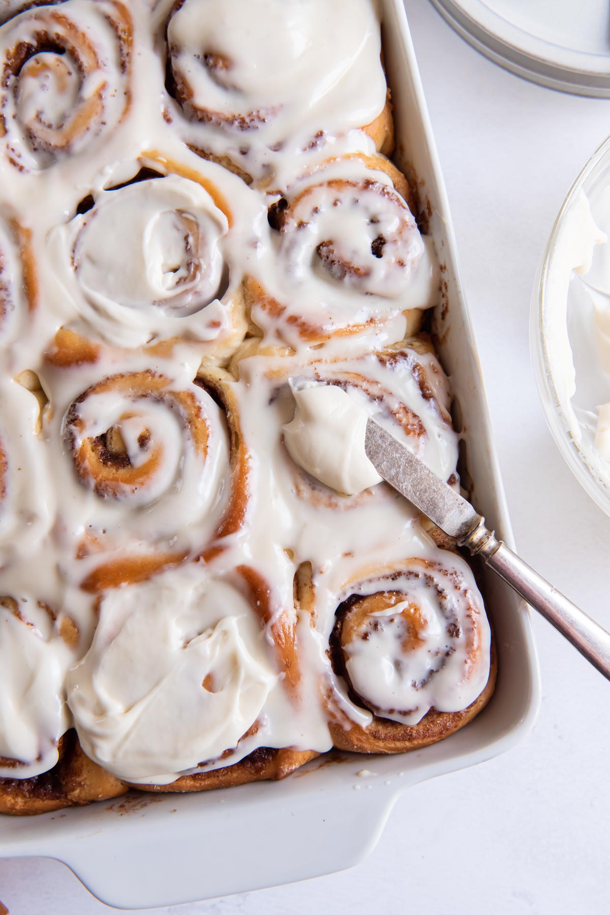 Spreading cream cheese frosting on baked cinnamon rolls.