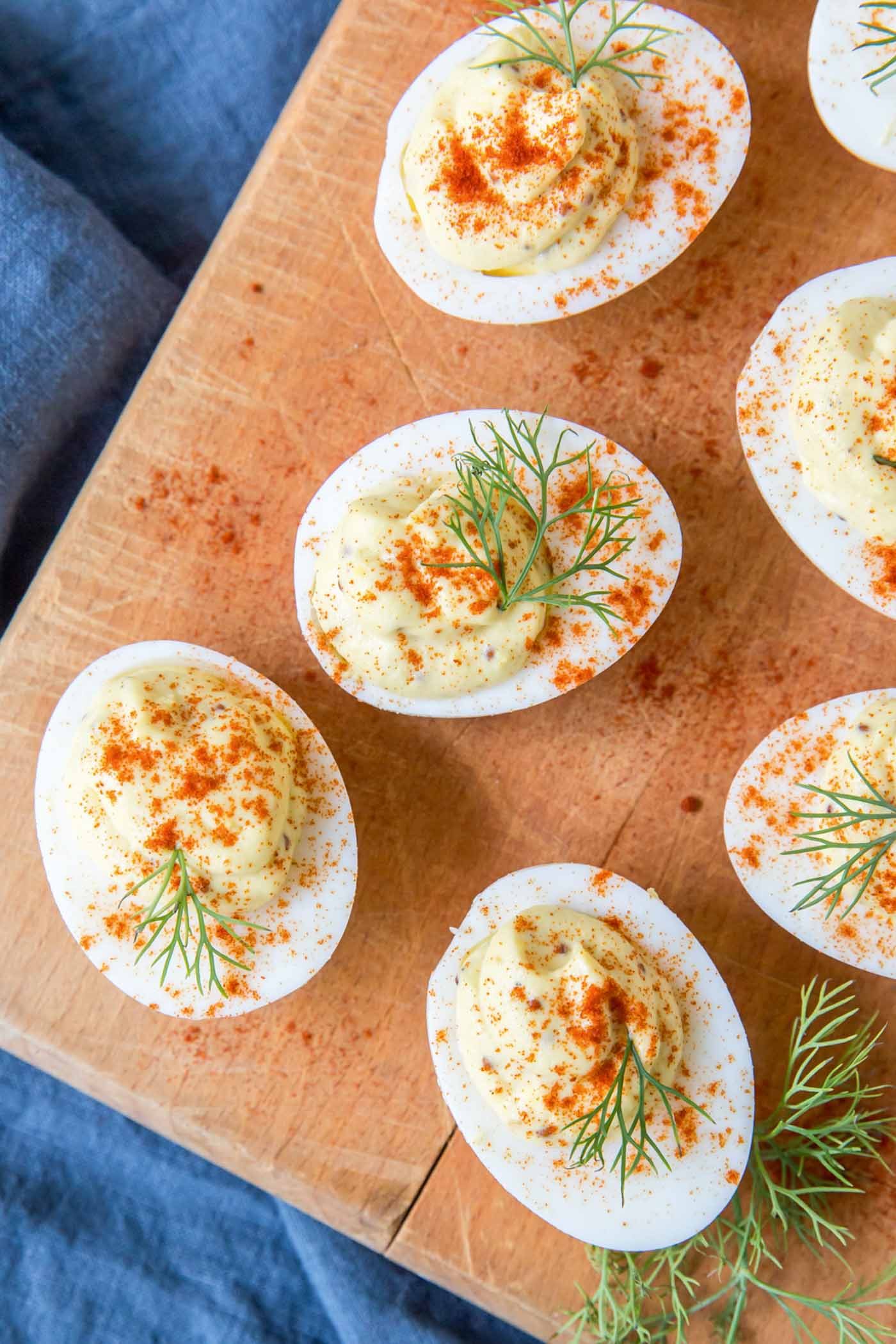 Close up of deviled eggs with paprika sprinkle and fresh dill garnish on a wood board.