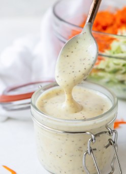 Coleslaw dressing dripping off of a spoon into a jar of dressing.