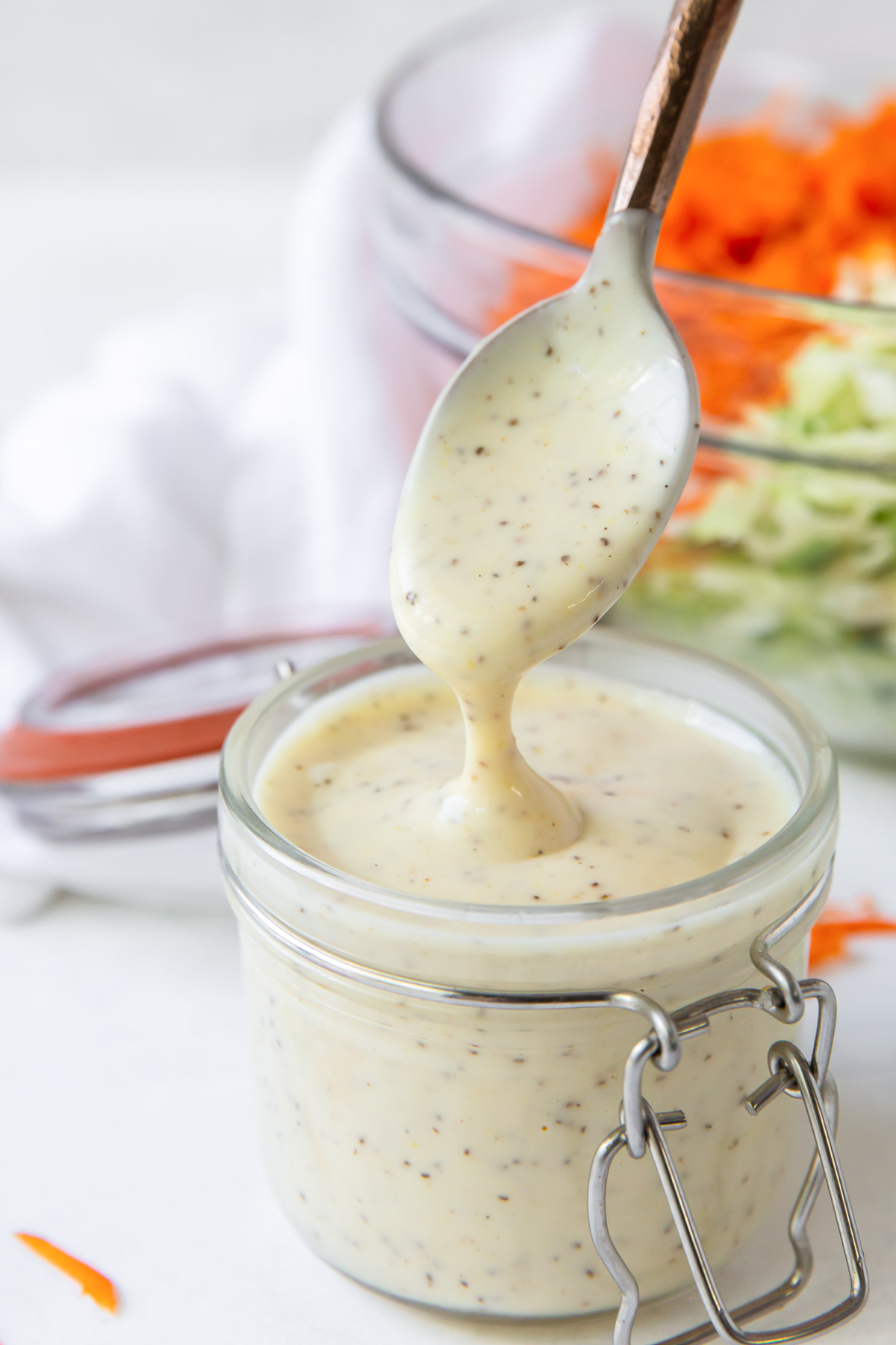 Coleslaw dressing dripping off of a spoon into a jar of dressing.