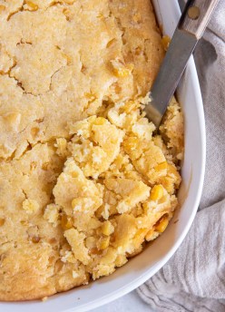 Corn casserole in baking dish with serving spoon.