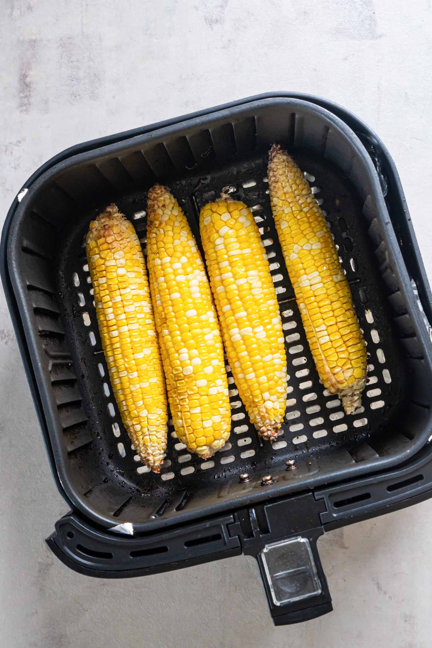 Four cooked ears of corn in an air fryer basket.
