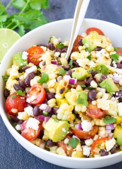Corn salad with black beans, avocado and tomatoes in a white serving bowl with a spoon.