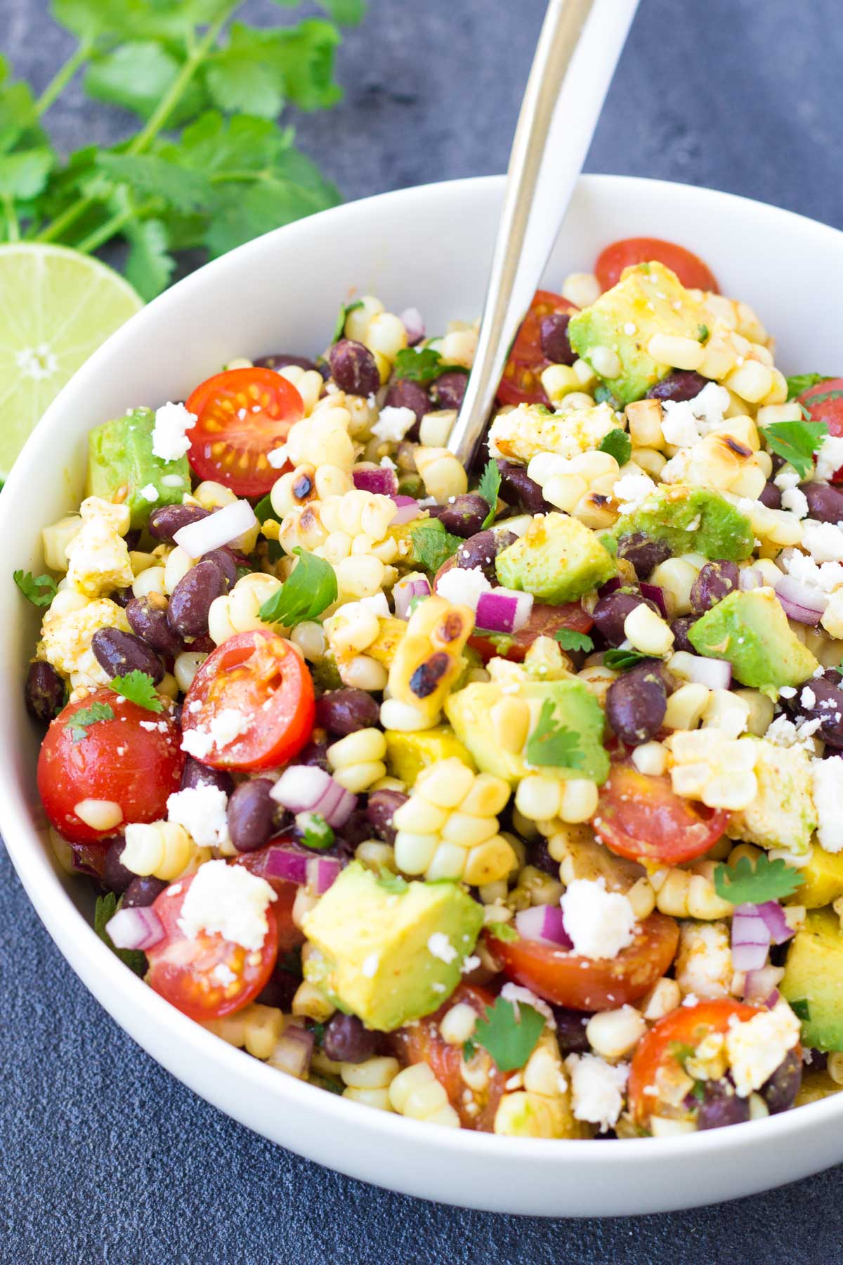 Corn salad with black beans, avocado and tomatoes in a white serving bowl with a spoon.