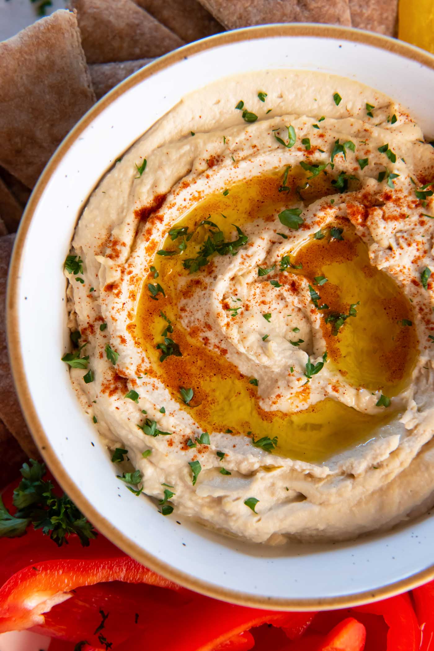 Hummus served in a bowl, garnished with olive oil, paprika and fresh parsley.